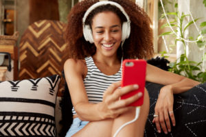 mulher jovem com cabelo afro fazendo uma chamada de vídeo pelo celular usando headphones