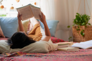 garota morena segurando livro acima da cabeça deitada da cama