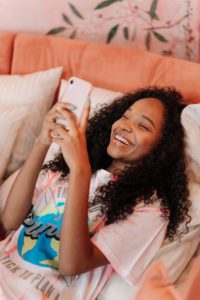 garota jovem negra maquiada vestindo rosa sorrindo para o celular 