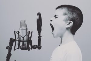 criança cantando em frente a um microfone em preto e branco