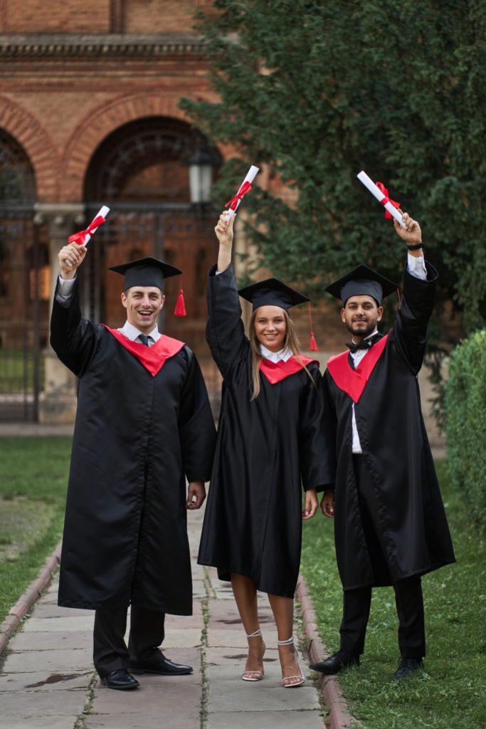 Estudantes formados erguendo os diplomas na formatura para a diferença de licenciatura e bacharelado