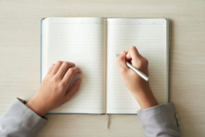 Visão de cima de caderno em branco com mãos apoiando caneta