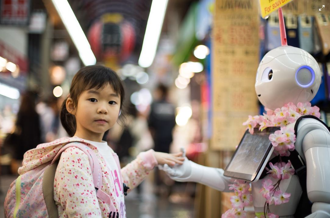 Criança asiática segurando as mãos de um robô, fazendo àlusão à Inteligência Artificial na educação