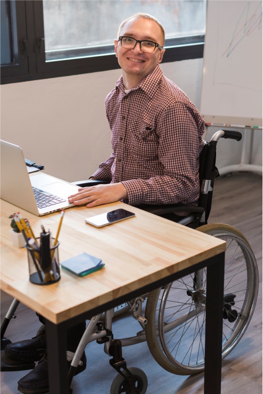 Homem de cadeira de rodas no trabalho, em frente a um computador