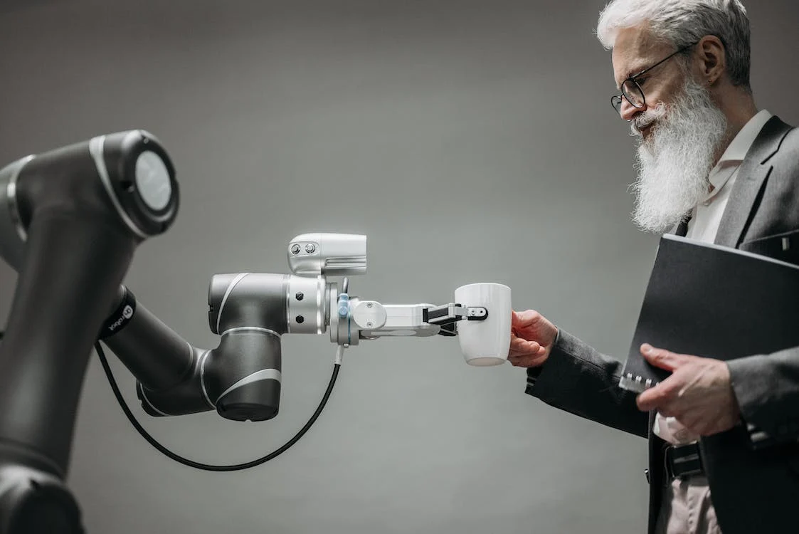 Homem idoso segurando uma xícara e uma um robô
